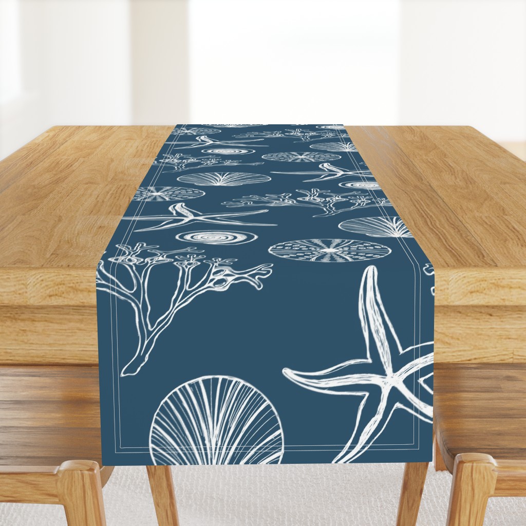 Moch up of a table runner with a blue and white coastal design of starfish, seaweed, periwinkles, and sea urchins on a light wood table.